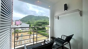 A balcony with a view of a hillside and buildings. - 6-49 - 1 Bdr Condo With Balcony and Shared Pool (Patong)