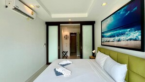 Habitación de hotel con cama, mesita de noche, televisor de pared mostrando una escena de playa y un equipo de aire acondicionado.