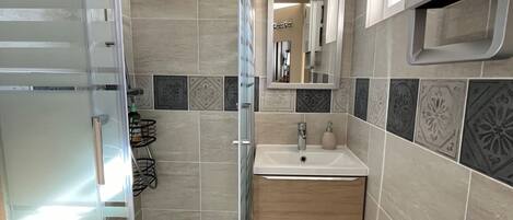 A modern bathroom with a glass shower enclosure, a sink with a mirror, and a vanity with drawers.