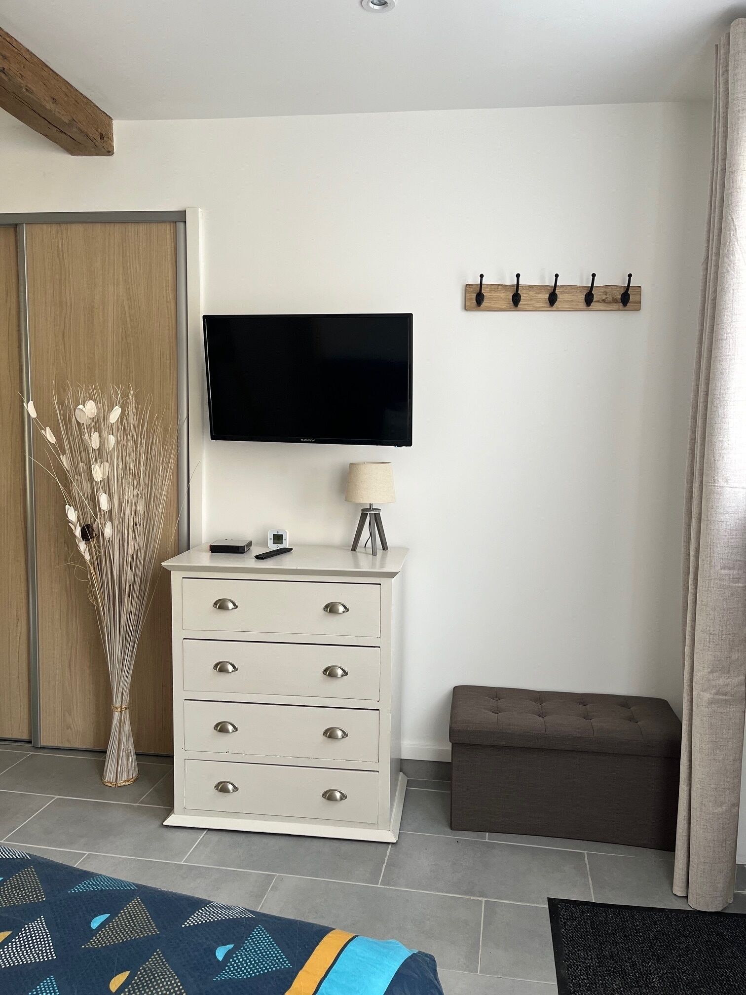 A modern living room with a flat-screen TV, a white dresser, a bench, and a decorative vase.