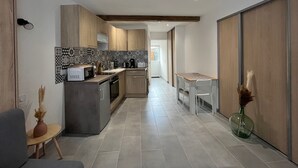 Una cocina moderna con microondas, estufa y pileta. Hay una mesa de comedor con sillas y un florero con plantas secas. La cocina tiene un salpicadero de azulejos y muebles de madera.