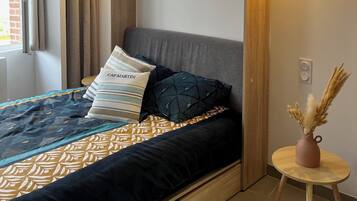 Una camera da letto moderna con un letto, una testiera in legno, un piccolo tavolino con un vaso e una finestra con tende.