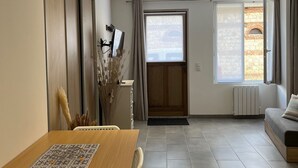 Una sala de estar moderna con una mesa de comedor de madera, un sofá y vistas a un edificio de piedra a través de un ventanal grande.