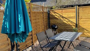 En terrasse med et bord, stole og en blågrøn parasol, samt et træhegn.