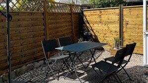 Un patio con mesa y sillas, una parrilla y un gran paraguas.