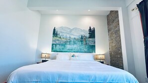 Una cama grande con ropa blanca, dos lámparas de noche y un cuadro con paisaje de montaña en la pared.