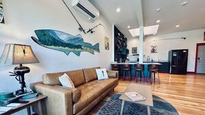Una sala de estar moderna con un sofá de cuero marrón, una mesa de centro y una alfombra. Hay una zona de cocina con un refrigerador y una barra.