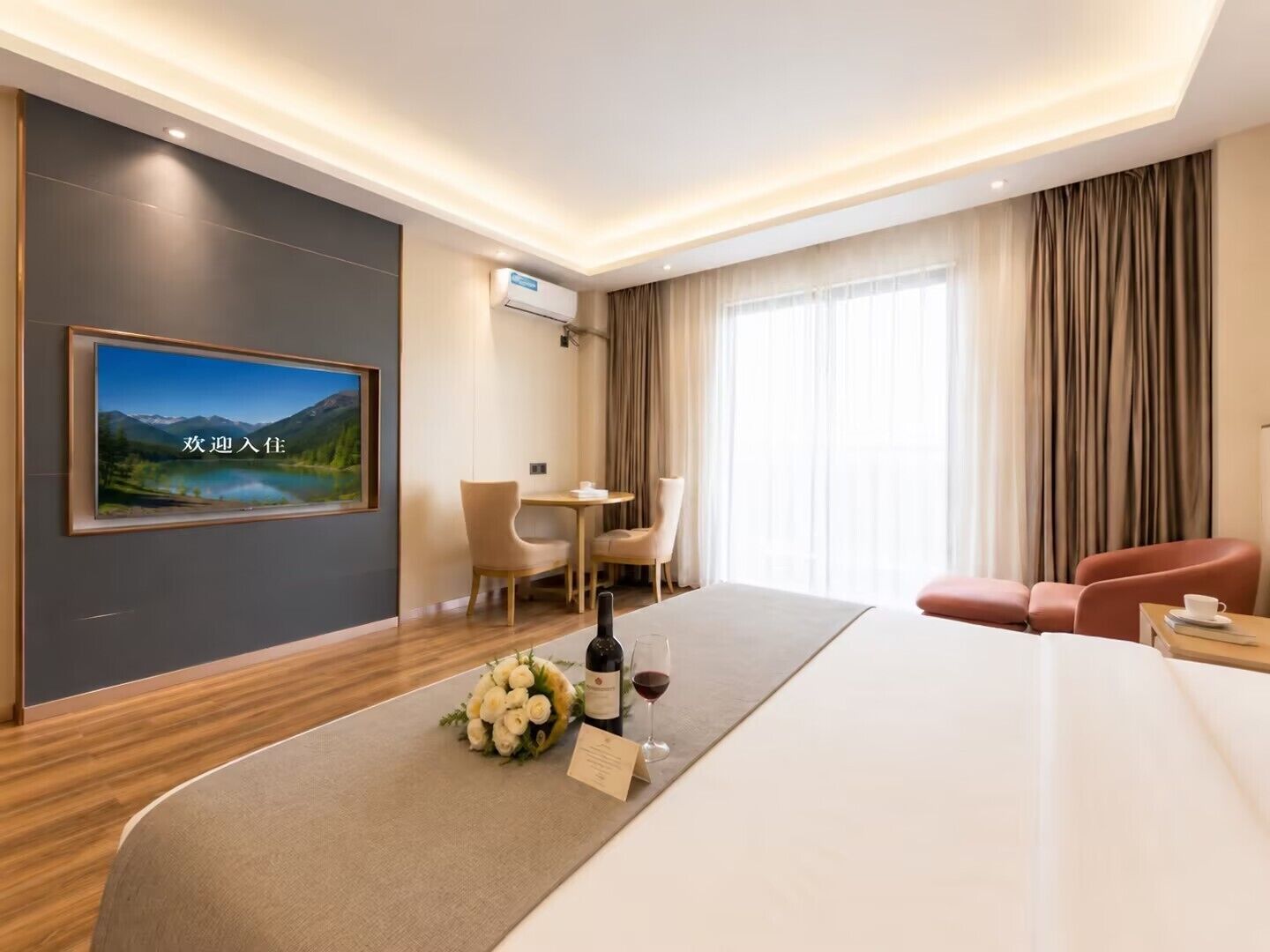 Una camera d'hotel con un letto, una scrivania, una sedia, una TV a parete e una finestra con tende.