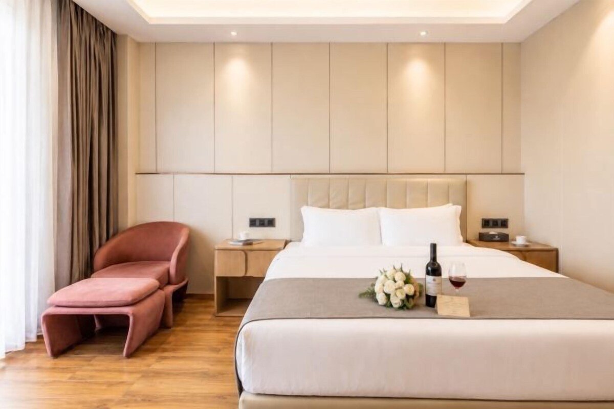 Une chambre d’hôtel avec un lit, des tables de chevet, une chaise et une bouteille de vin.