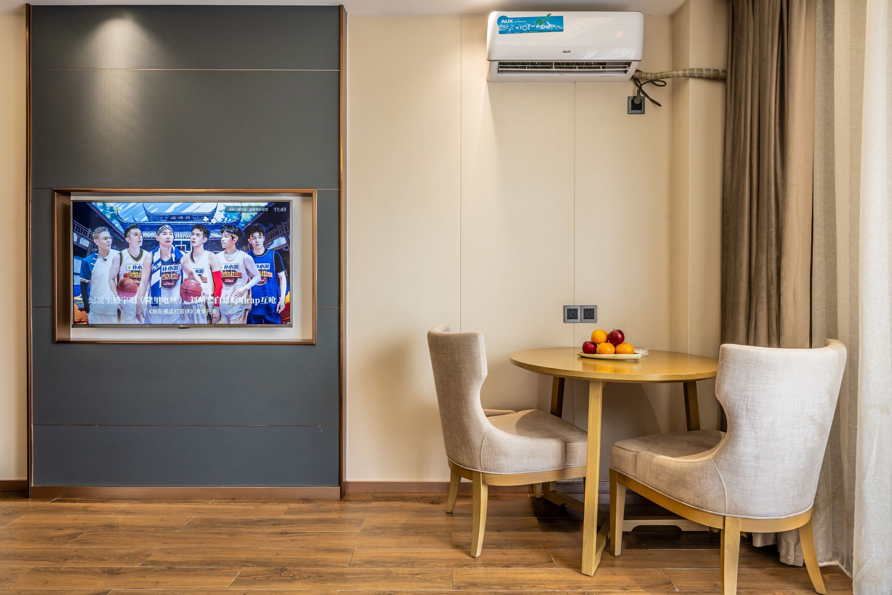 A hotel room with a framed sports team photo, a round wooden table with two chairs, and an air conditioning unit on the wall.