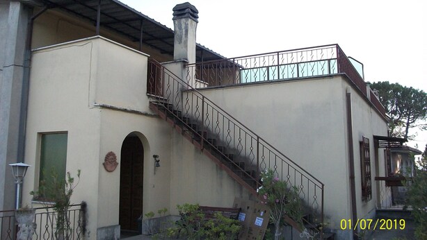 Un edificio con una escalera que lleva a un balcón, una puerta y un pequeño jardín.