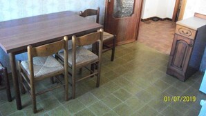 Un comedor con una mesa de madera y cuatro sillas, una puerta con un panel de vidrio esmerilado y un mueble pequeño.