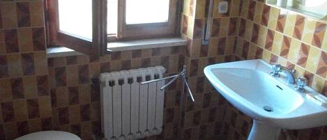 Une salle de bain équipée de toilettes, d’un lavabo, d’une fenêtre et d’un radiateur.
