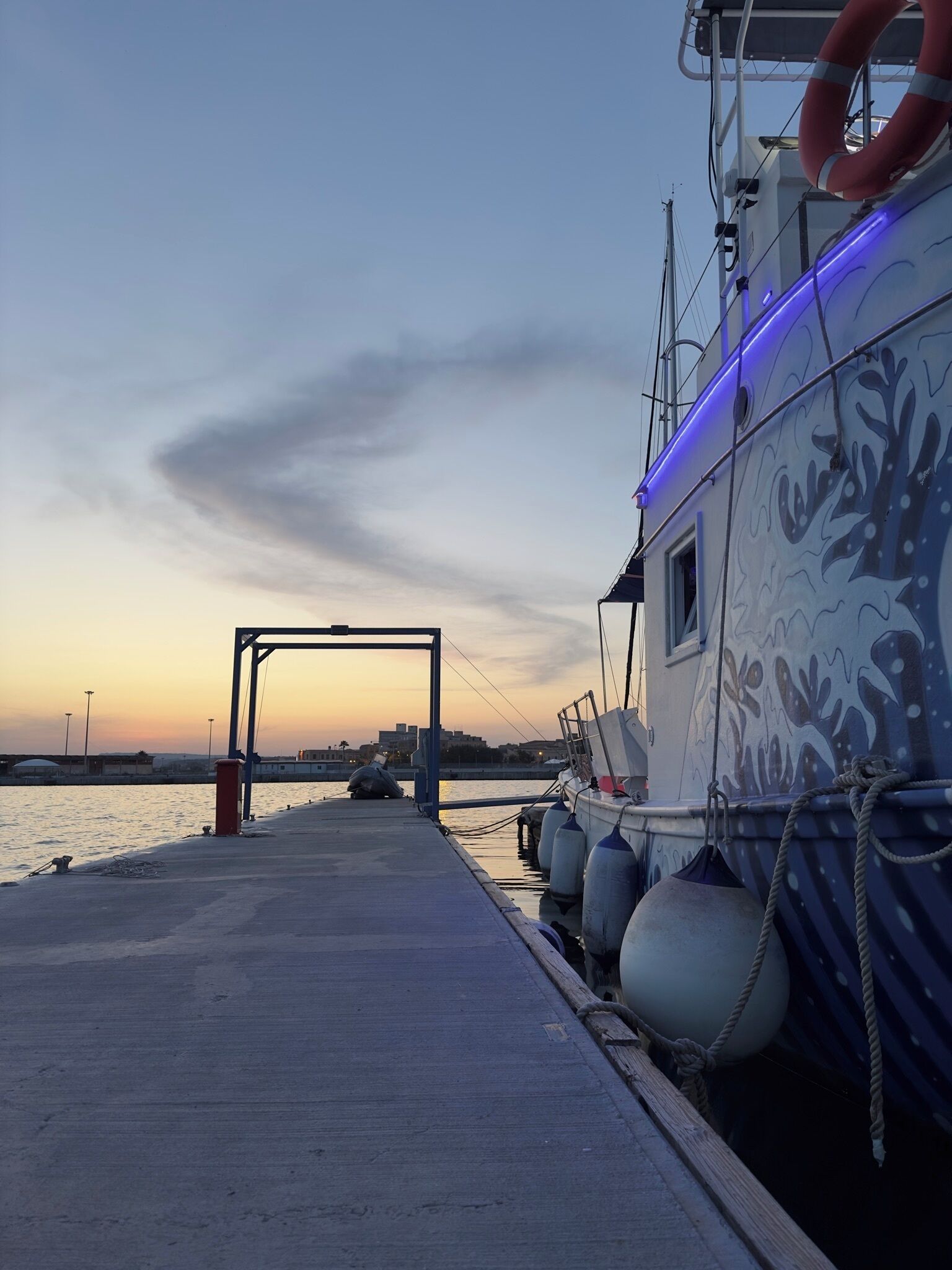 Une jetée avec un bateau amarré, sur laquelle on peut voir une bouée de sauvetage, des cordes et un ciel dégagé.