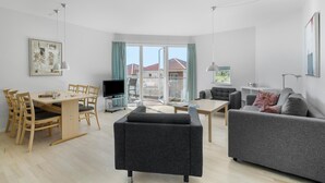 A modern living room with a dining area, grey sofas, a coffee table, and a TV. - Gudhjem Søpark Lejl. 12 (Gudhjem)