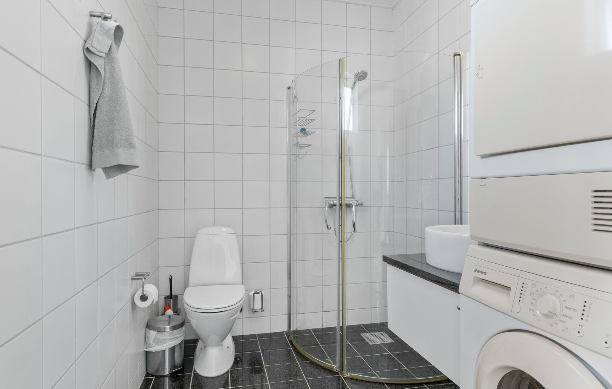Et moderne badeværelse med toilet, brusebad med glasvægge og en vaskemaskine.