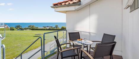 A balcony with a table and chairs, overlooking a grassy area and the sea.