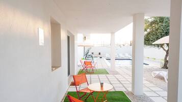 Ein Korridor mit künstlichem Gras, der zu einem Poolbereich führt, mit einer Reihe orangefarbener Stühle und einem weißen Sonnenschirm.