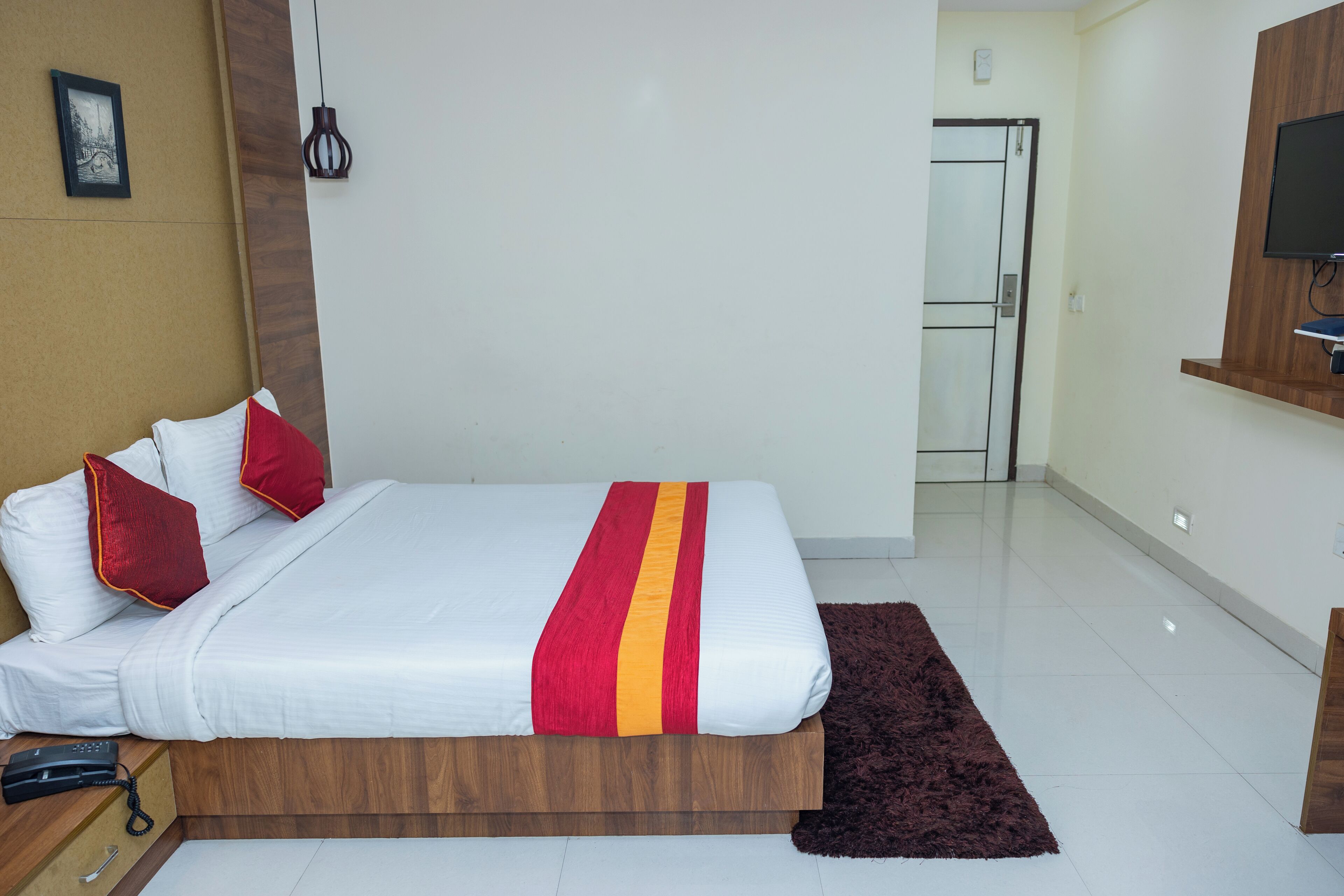 A hotel room with a bed, a wooden headboard, a telephone, a brown rug, and a television on the wall.