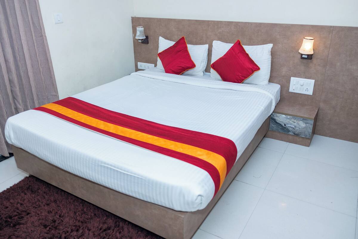 A neatly made bed with a white and red striped blanket, two red pillows, and a headboard with wall-mounted lights.