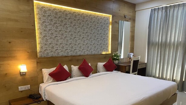 A modern hotel room with a large bed, bedside tables, a wall-mounted light, and a mirror. - Ishwerya Suites (Bengaluru)