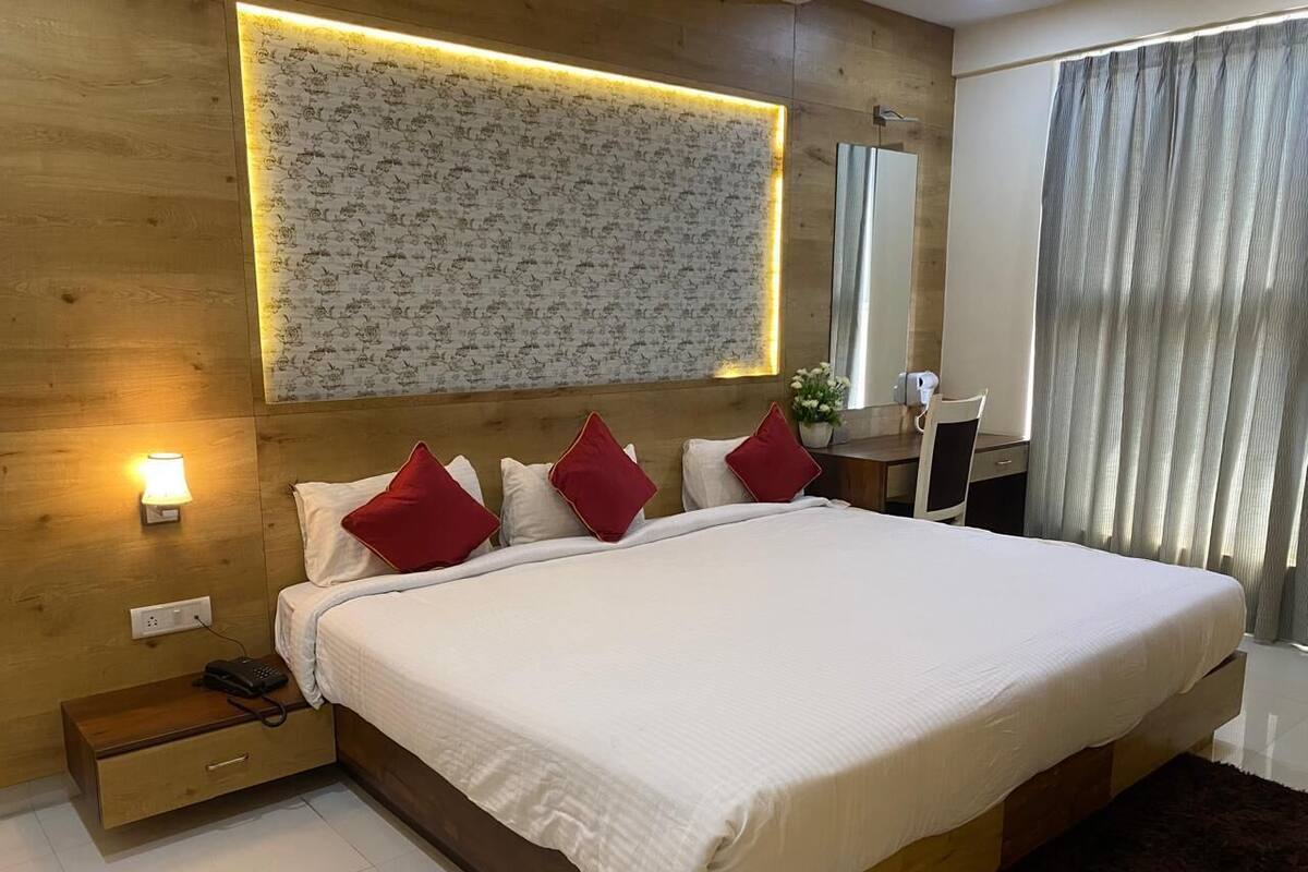 A modern hotel room with a large bed, bedside tables, a wall-mounted light, and a mirror.