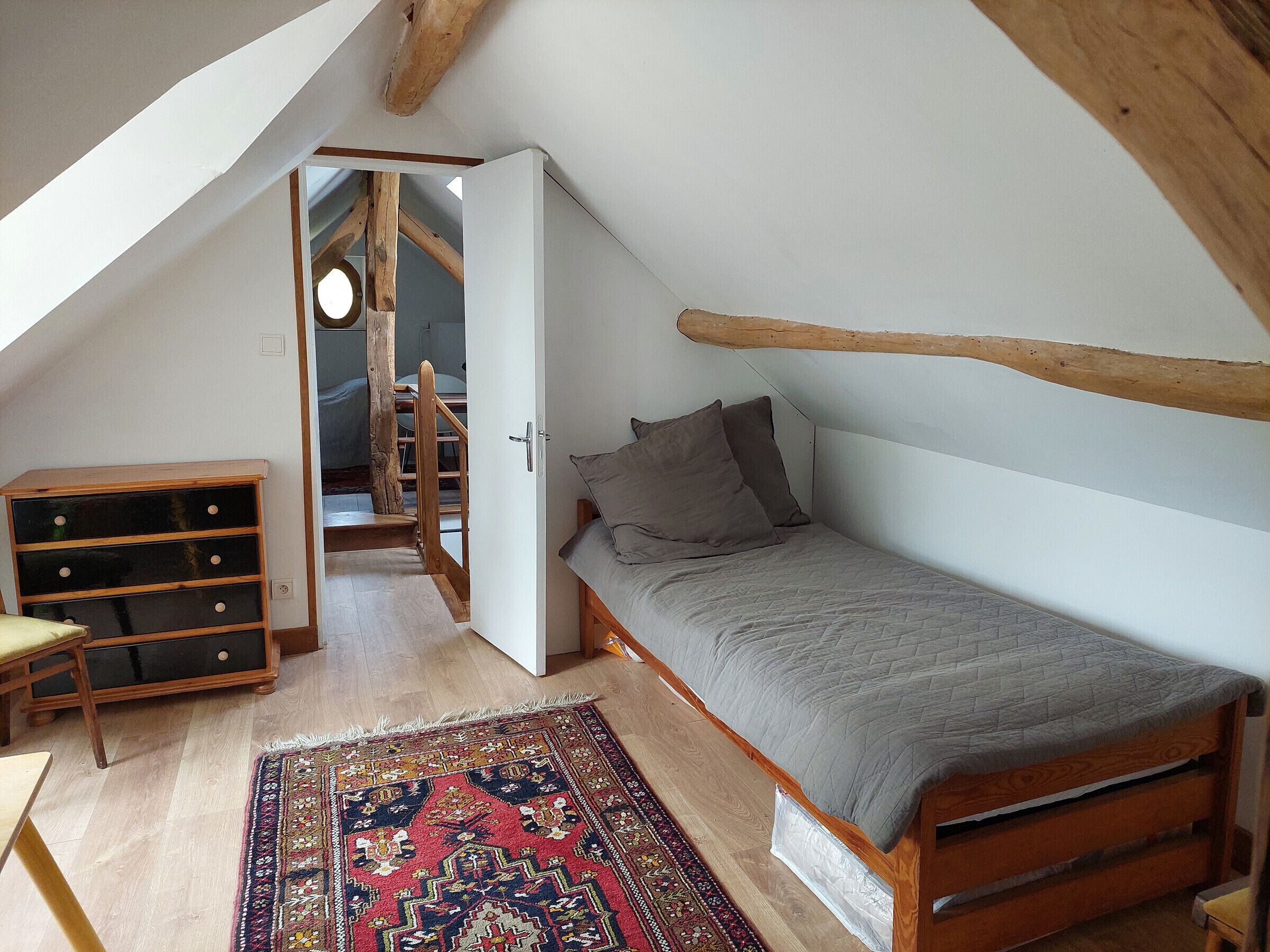 Une chambre mansardée chaleureuse, avec un lit, une commode en bois et un tapis coloré.