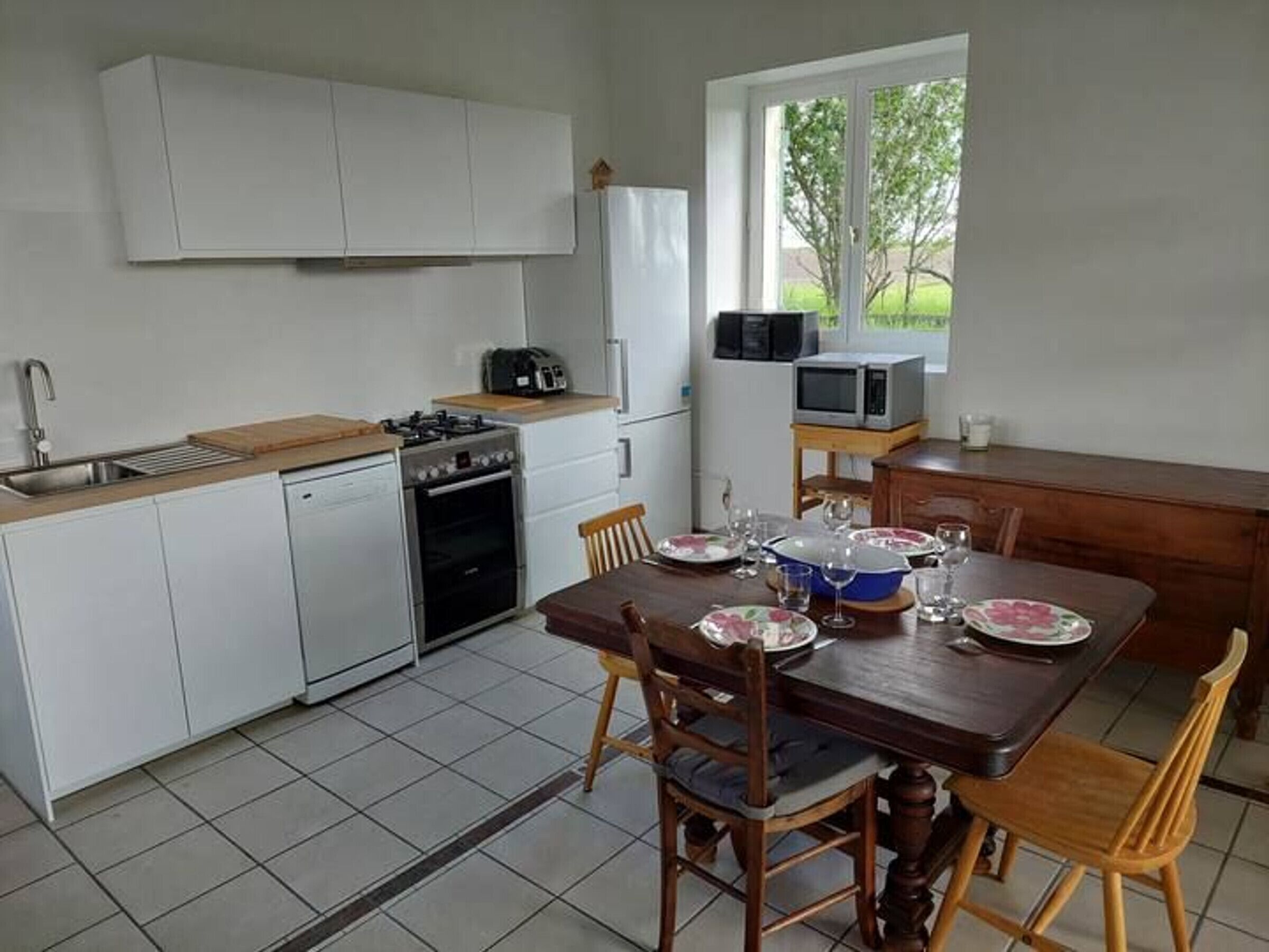A compact kitchen with white cabinets, a gas stove, a dishwasher, and a window with a view of greenery.