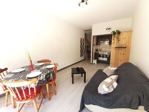 Un espace de vie compact comprenant une table à manger pour quatre personnes, un canapé, un petit coin cuisine et un escalier menant à un lit en mezzanine.