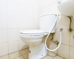 Eine weiße Toilette mit Tank und Bidetanschluss in einem gefliesten Badezimmer.