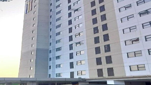 A tall building with multiple windows and a person standing in front of a parked car. - OYO 94087 Apartemen 19 Avenue By Rh (Jakarta)