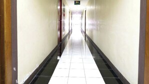 A long, narrow hallway with a black and white tiled floor, beige walls, and doors on both sides. - OYO 94087 Apartemen 19 Avenue By Rh (Jakarta)