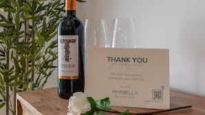 A bottle of Tiberio wine, a thank you card, and a white flower on a wooden surface.