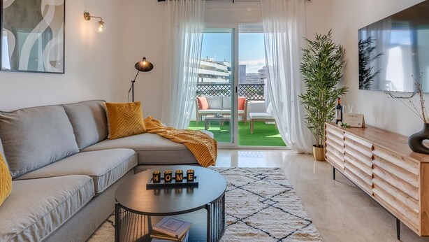 A modern living room with a grey sofa, a round coffee table, and a TV mounted on the wall. - Luxury 2BR Apt in Heart of Puerto Banús – Steps from Beach with Mountain Views (Marbella)