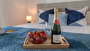 A bed with a wooden tray holding a bottle of vintage Codorniu champagne and a bowl of strawberries. - Luxury 2BR Apt in Heart of Puerto Banús – Steps from Beach with Mountain Views (Marbella)