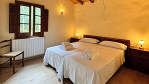 A bedroom with two beds, wooden beams on the ceiling, a window with shutters, a chair, and bedside lamps. - More Morrenyà - Rural House Garrotxa (Sant Jaume de Llierca)