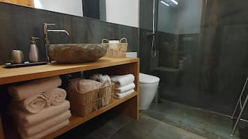 Ett modernt badrum med ett handfat i trä, en stor spegel, en duschvägg i glas och prydligt hopvikta handdukar på en hylla.