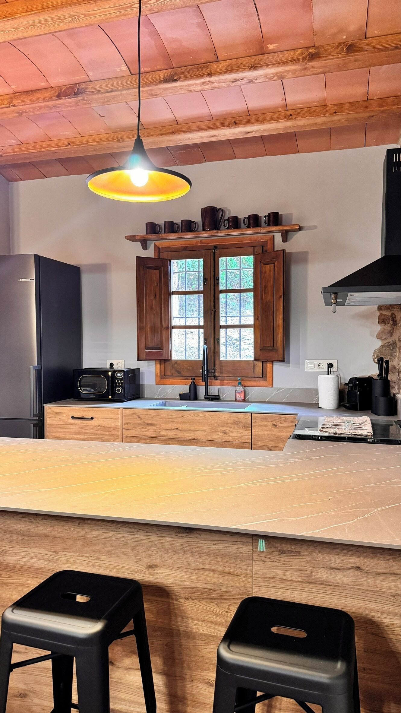 Een moderne keuken met houten kasten, een inbouwmagnetron en een groot keukenblok met krukken.