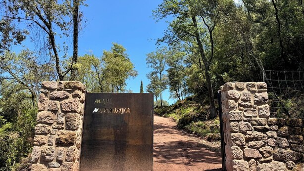 A stone gate with a metal plaque reading "MAS NERONA" in a natural setting with trees and a clear sky. - More Morrenyà - Rural House Garrotxa (Sant Jaume de Llierca)