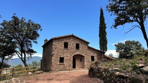 A stone building with a central entrance and two windows on the upper floor, surrounded by trees and a clear sky. - More Morrenyà - Rural House Garrotxa (Sant Jaume de Llierca)
