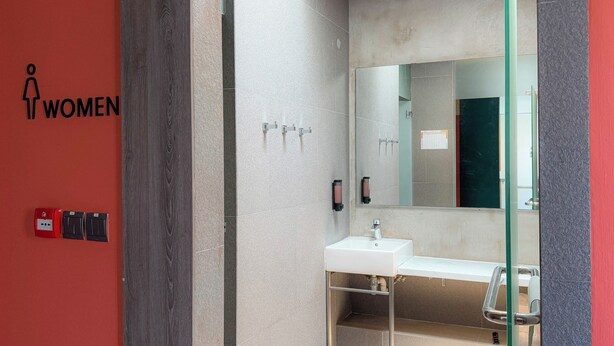 Une salle de bain moderne avec un lavabo blanc, un grand miroir et un mur rouge orné du symbole féminin.
