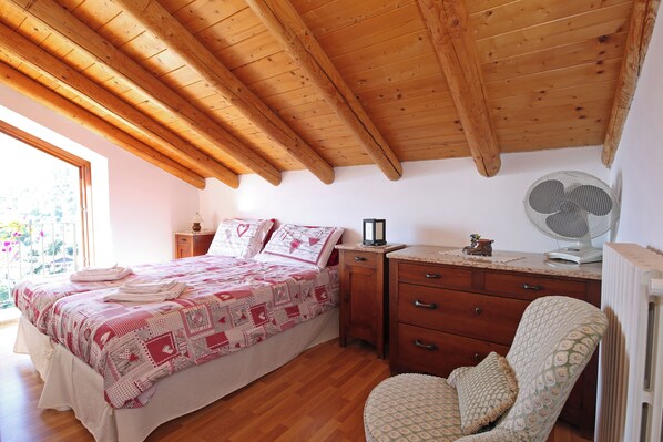 A bedroom with a wooden ceiling, a bed with a quilt, a bedside table, a chair, and a radiator. - Ca' del Doss by Wonderful Italy (Bellagio)