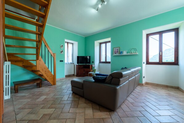A spacious living room with a wooden staircase, a sofa, a television, and large windows. - Ca' del Doss by Wonderful Italy (Bellagio)