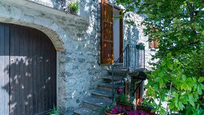 A stone building with a wooden door, a staircase leading to a balcony with potted plants, and a small garden area. - Ca' del Doss by Wonderful Italy (Bellagio)