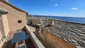 A terrace with a table and chairs, overlooking a coastal town with stone buildings and a view of the sea. - Fisherman's house in the little port (Cagnano)