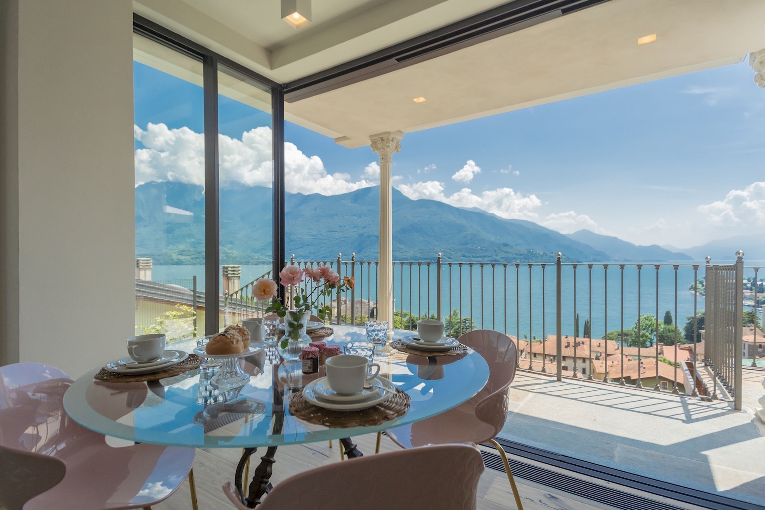 A glass table with white cups and pastries, overlooking a mountainous landscape.