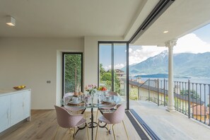 Ein Essbereich mit einem Glastisch, rosa Stühlen und Blick auf Berge und einen See.