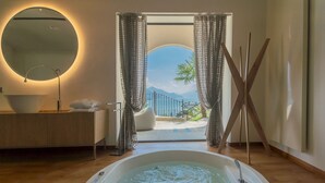 Un bagno con vasca, uno specchio rotondo, un lavandino e vista su un balcone con una palma.