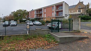 Parkkipaikka, jossa on useita autoja, parvekkeellinen rakennus ja portilla varustettu sisäänkäynti.