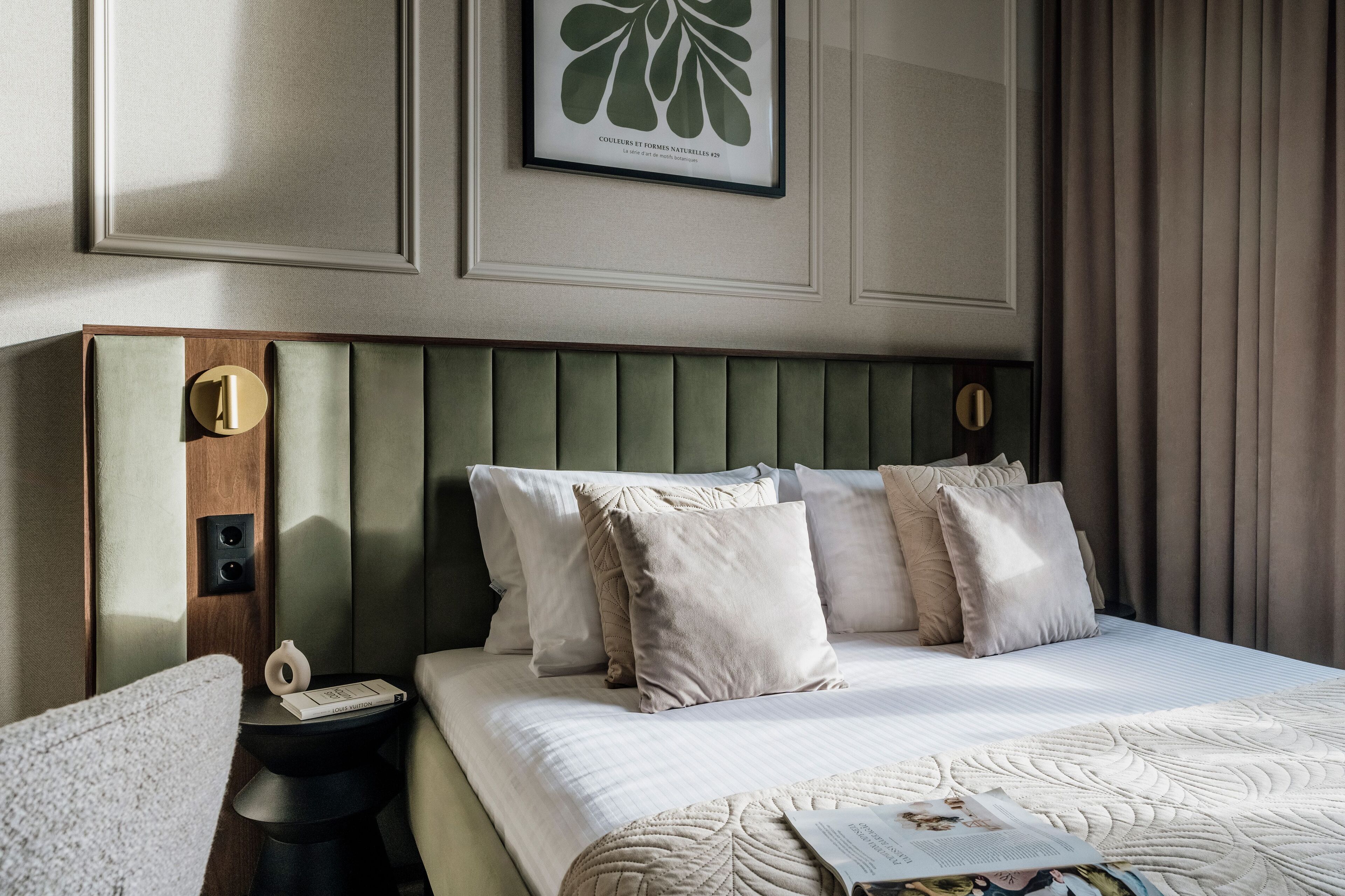 A neatly arranged hotel room with a bed, pillows, a bedside table, and a framed artwork on the wall.